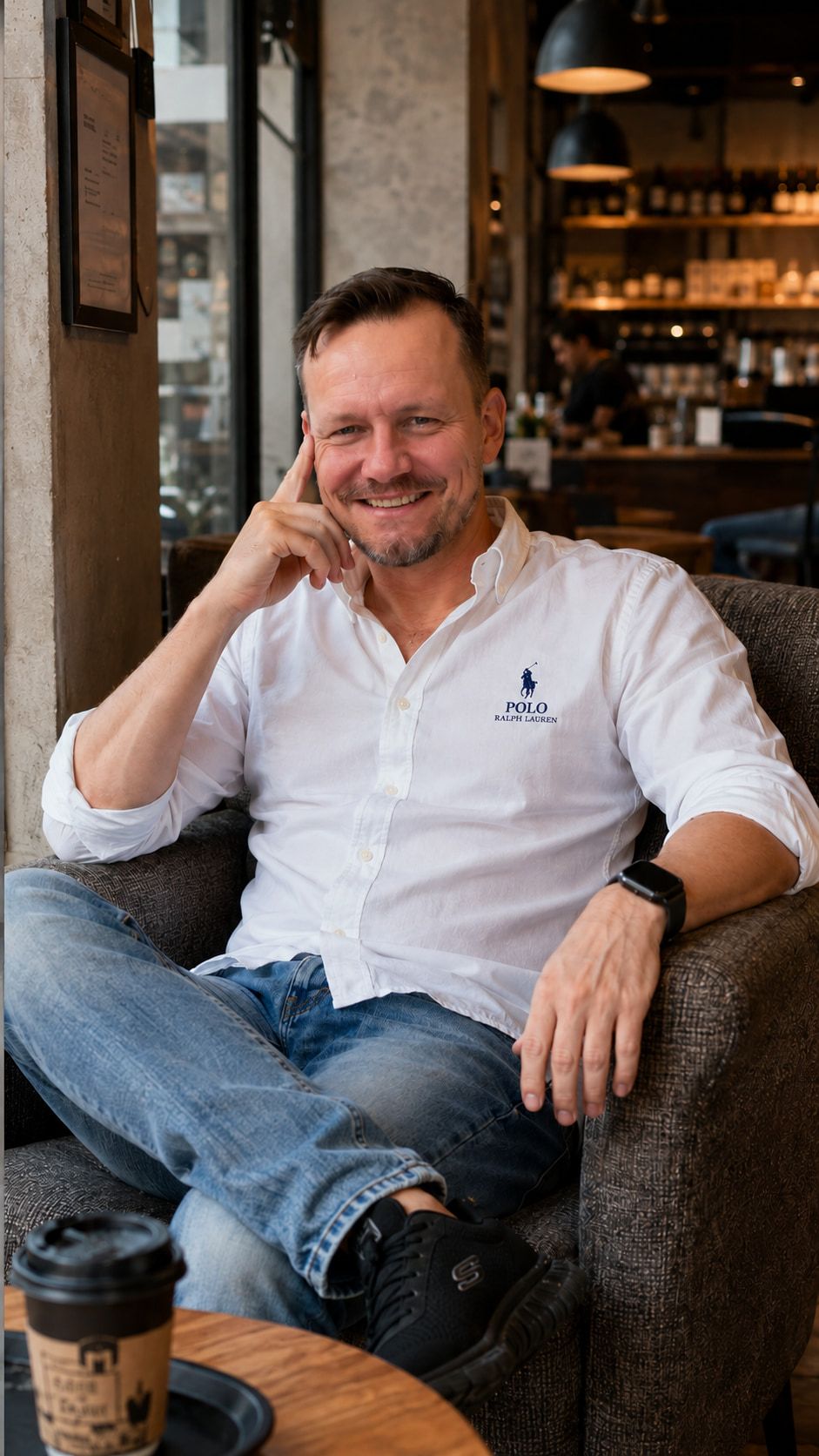 Jan Rolfsmeyer sitzt entspannt in einem Sessel in einem Café, ein Kaffeebecher steht auf dem Tisch.